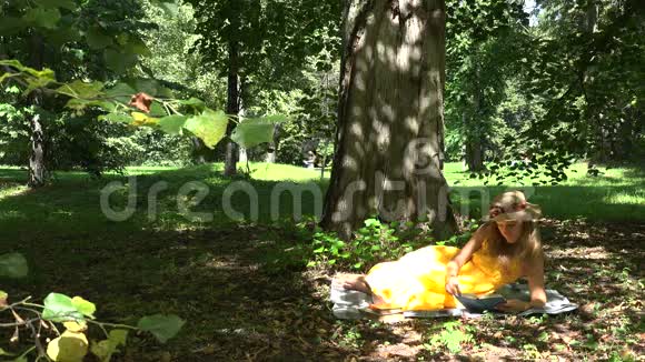 在阳光明媚的夏日女人躺在格子呢上在公园里看书4K视频的预览图