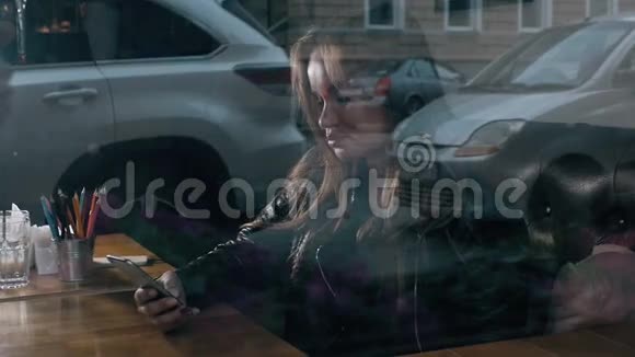 在咖啡厅使用电话的年轻女性从窗口观看城市广场视频的预览图