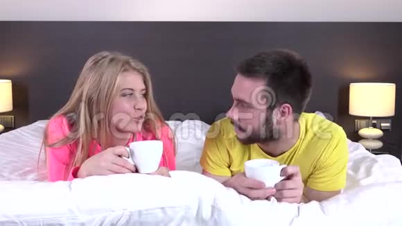 微笑的情侣躺在床上喝着咖啡特写镜头视频的预览图