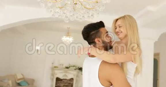 年轻的幸福夫妇拥抱女人奔跑跳过男人拥抱旋转在现代的家庭卧室盘旋视频的预览图