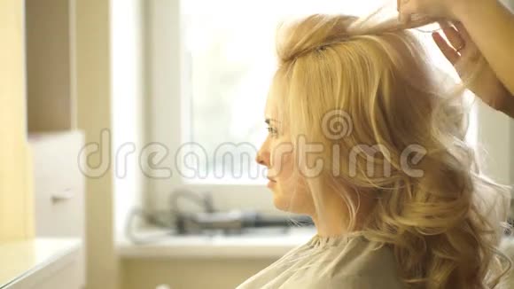 美容师在美容院为商务女性的金发做晚间发型特写视频的预览图