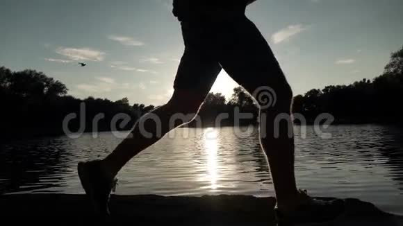 超级慢动作稳定夹男性跑步者日落剪影对水视频的预览图