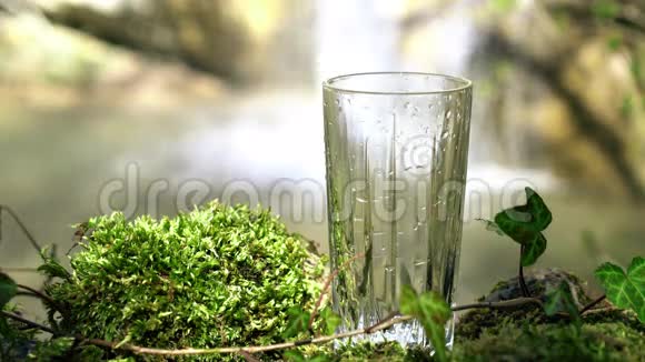 玻璃饮用天然水与瀑布在柔和的焦点背景从泉水中流出的纯净生态水视频的预览图