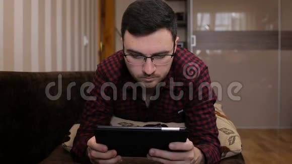 年轻人躺在沙发上在平板电脑上获取短信视频的预览图