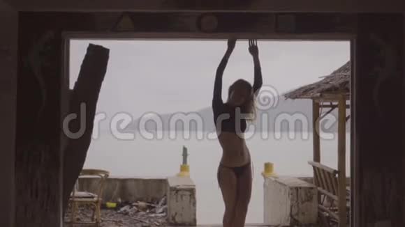 后景的金发女人穿着黑色优雅的泳衣站在露台窗户的废弃建筑在海上视频的预览图