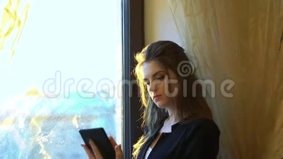 商务女士在窗户和窗帘的背景下使用智能手机视频的预览图