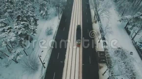 在冬季森林道路上的顶部可以看到汽车和电车雪花空中无人机镜头视频的预览图