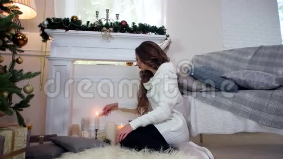 冬天女孩点燃了一支蜡烛坐在圣诞树附近的壁炉旁美丽的年轻女子在温暖舒适的环境中视频的预览图