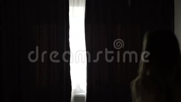 迷人的年轻女子拉开窗帘看着日出站在她家的窗户附近享受着城市的乐趣视频的预览图