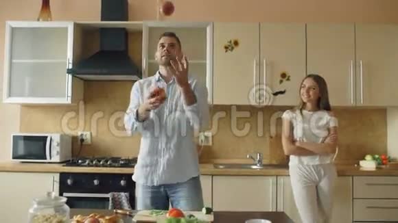 可爱的情侣在厨房里玩得很开心英俊的男人拿着苹果来讨好他的女朋友视频的预览图