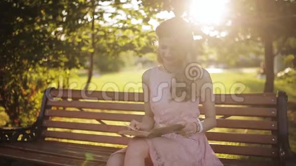 年轻女子坐在公园的长凳上看书一个漂亮的欧洲女孩带着书在学视频的预览图