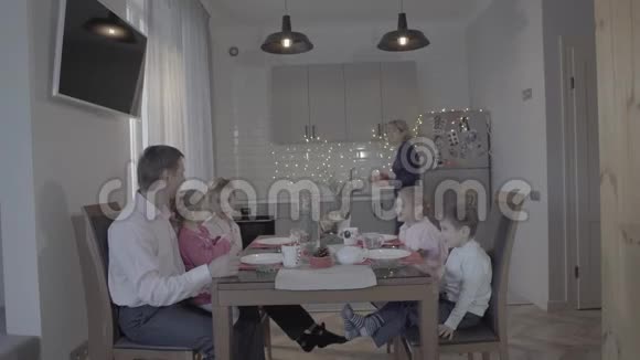 可爱快乐的四个孩子一家人庆祝新年厨房餐桌父亲儿子女儿微笑的母亲端饭视频的预览图