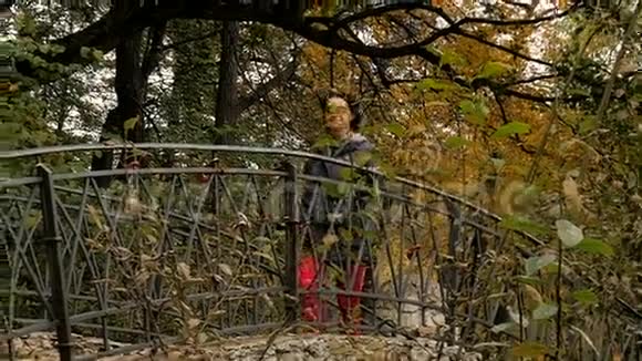 一个女人走在公园里穿过老桥阳光明媚的秋日视频的预览图