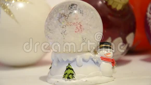 圣诞装饰品雪落在闪闪发亮的神奇水晶球里背景是雪人和圣诞球白雪覆盖的穹顶视频的预览图
