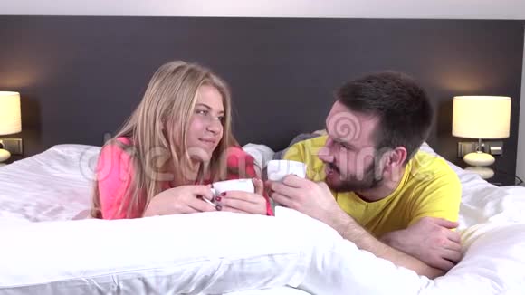 微笑的情侣躺在床上喝着咖啡特写镜头视频的预览图