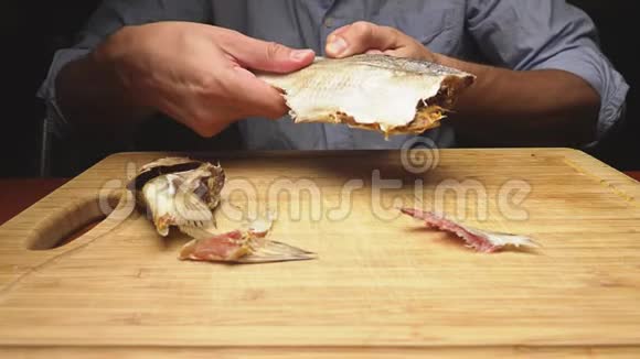 特写镜头男性手清洁咸干鱼在切割板上4K慢动作视频的预览图