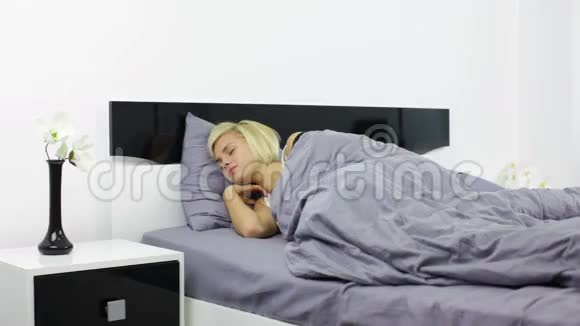 年轻迷人的女人醒来在床上伸展视频的预览图