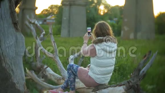 一位年轻女子正在一座老式铁路桥附近使用智能手机视频的预览图
