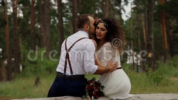 奢华幸福的新娘和时尚的新郎坐在夏日森林的原木上视频的预览图