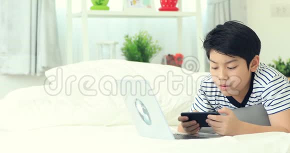 可爱的亚洲男孩手里拿着智能手机和打字机脸上带着微笑视频的预览图