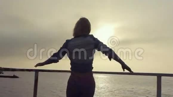 日落时分年轻女子在海边的码头上跳舞视频的预览图