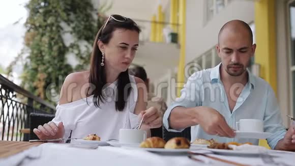 年轻夫妇在户外咖啡馆的一张桌子上吃早餐和聊天视频的预览图