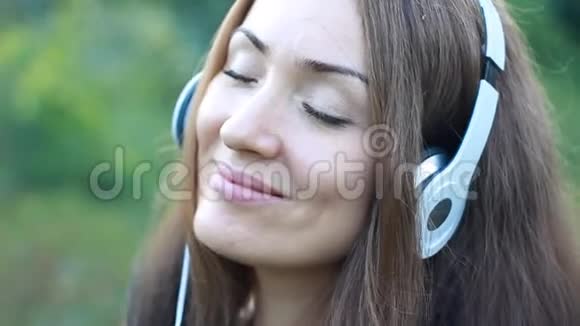 女人在户外用耳机听音乐一个漂亮的特写女孩的肖像视频的预览图