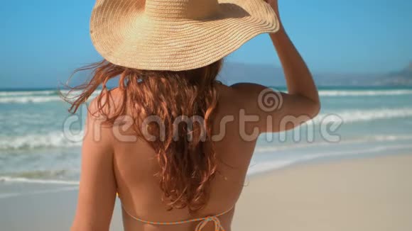穿着比基尼戴着帽子站在沙滩上阳光明媚的年轻白人女性视频的预览图