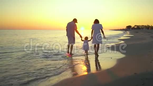 家人在海滩上散步父母和他们的小女儿沿着海滨散步他们握着手他们很开心视频的预览图