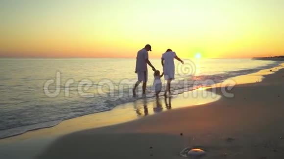 家人在海滩上散步父母和他们的小女儿沿着海滨散步他们握着手他们很开心视频的预览图