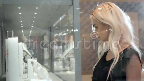 年轻的女人看着商店橱窗和珠宝看着它更近美丽的学生金发时装模特视频的预览图