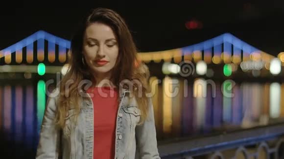 夜晚在城市里打电话的女孩照亮了背景桥和河水中的倒影视频的预览图