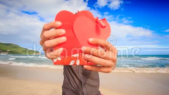 男子手持红心礼在海浪沙滩微笑视频的预览图