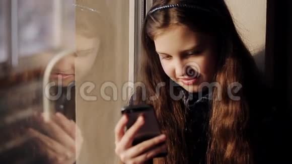 小女孩坐在窗边手里拿着电话视频的预览图