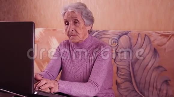 坐在沙发上用笔记本电脑打字的老年妇女金属笔记本电脑视频的预览图