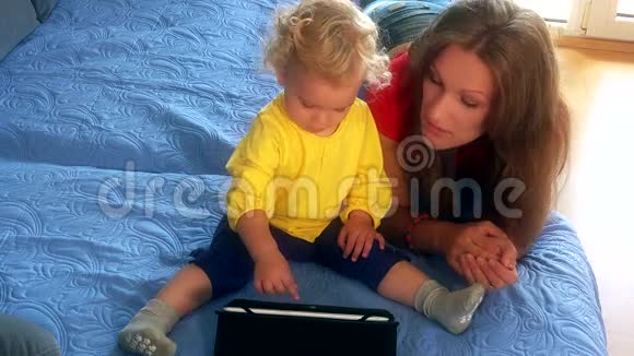 女人和她的小女儿在床上玩平板电脑视频的预览图