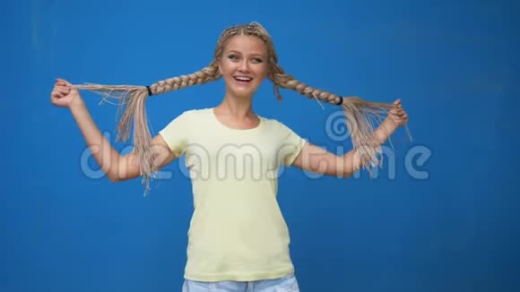 时髦的时髦女孩摇着辫子在蓝色背景下旋转视频的预览图