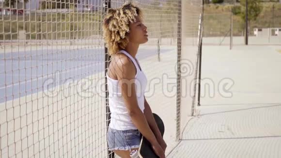 带滑板的年轻女子靠在栅栏上视频的预览图