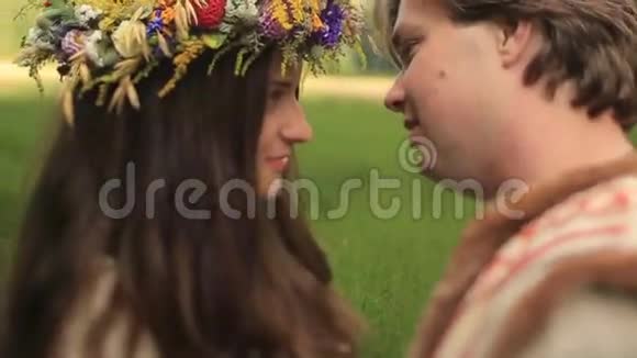 美丽的黑发女孩穿着传统的乌克兰衬衫戴着花圈在绿色的春天亲吻她的男朋友视频的预览图