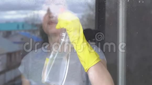 年轻女子戴着黄色手套用清洁剂洗窗户视频的预览图