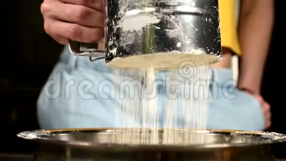 在家中的厨房里用金属碗中的筛杯特写一只雌性手筛面粉烹饪家庭烘焙视频的预览图