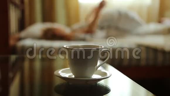 特写一杯热茶或咖啡年轻的女人早上醒来在床上伸展手臂模糊的焦点视频的预览图