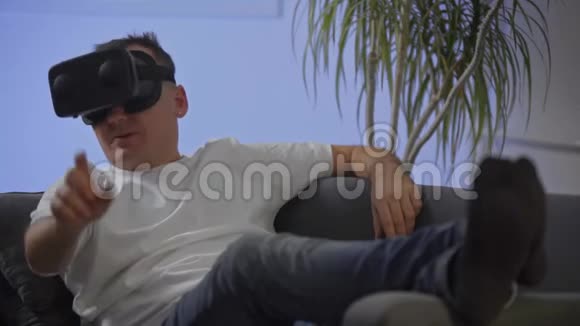 穿着白色衬衫的男人在沙发上享受虚拟现实谷歌视频的预览图