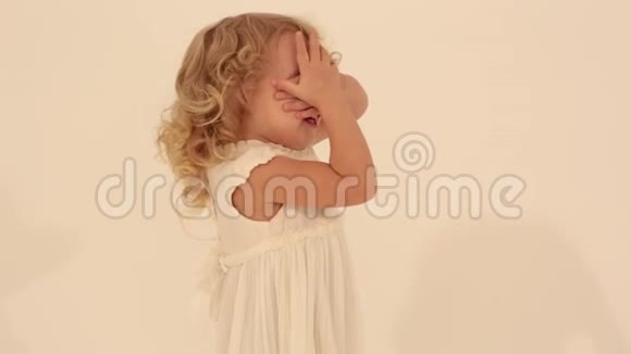 可爱的小可爱的小孩蹒跚学步的女孩金色卷发穿着白色连衣裙遮住眼睛玩捉迷藏视频的预览图