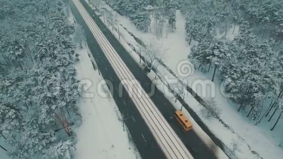 在冬季森林道路上的顶部可以看到汽车和电车雪花空中无人机镜头视频的预览图