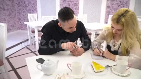 在咖啡馆里相爱的一对两个男人和女人在可爱的咖啡馆里聊天写在笔记本上视频的预览图