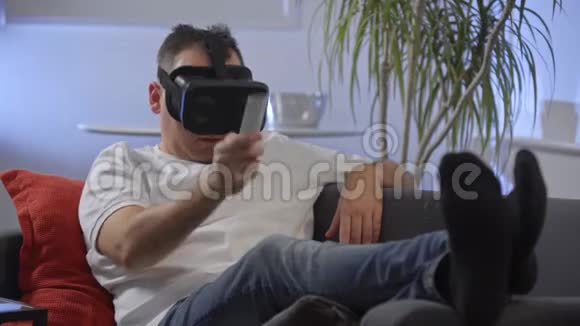 穿着白色衬衫的男人在沙发上享受虚拟现实谷歌视频的预览图