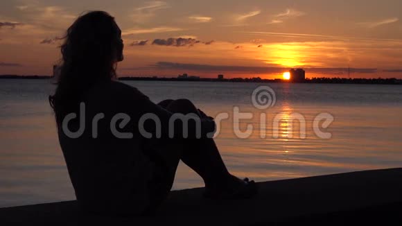 孤独的女人坐在码头上梦想和享受日落视频的预览图