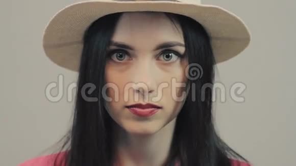 一幅美丽的年轻女子的肖像戴着夏天的帽子在阳光明媚的日子里在灰色的背景下看着相机眼睛闭上视频的预览图
