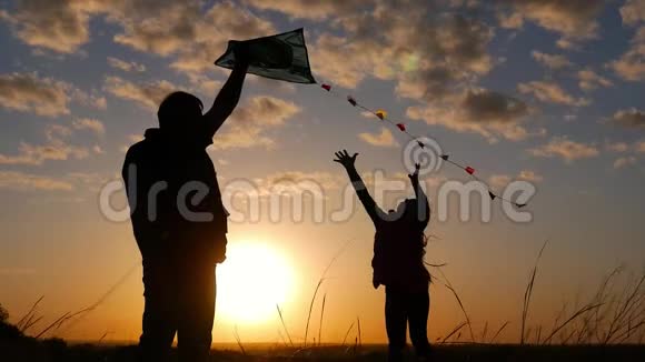 一个幸福的家庭玩风筝的剪影爷爷和小女孩在日落时玩风筝视频的预览图